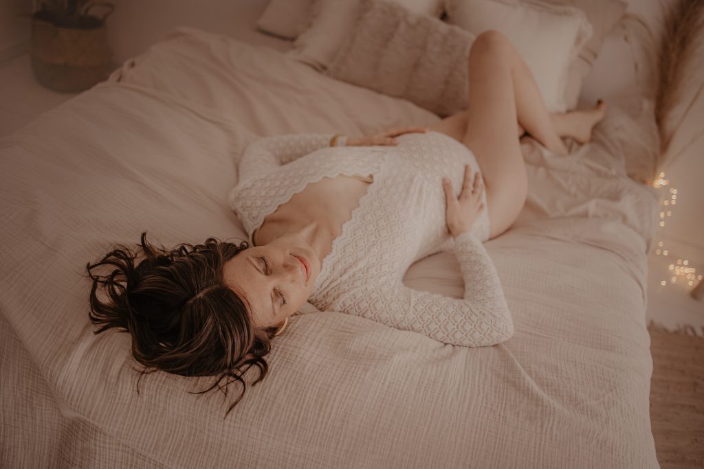 Future mman allongée sur un lit avec un body blanc